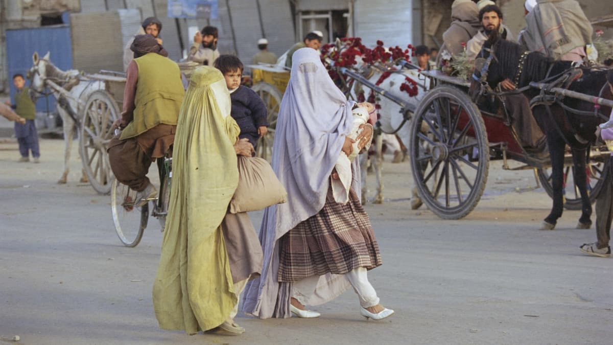 Kaksi afganistanilaista naista kävelee kadulla lapset sylissään.