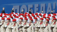 Nuoren armeijan jäsenet marssivat punaiset paretit päässään samanlaisissa puvuissa ja tukassa iso valkoinen ruusuke.