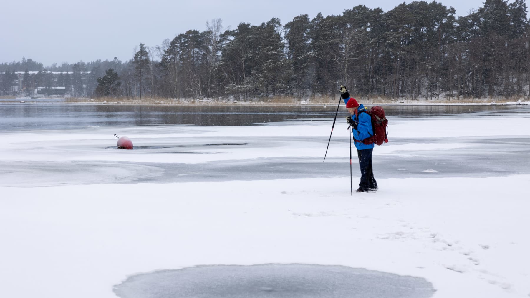 Tuomas Hannikainen seisoo jäällä, avovettä näkyy taustalla ja testaa rautakepillä jään kestävyyttä.