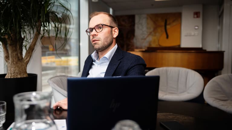 Mies istuu pöydän ääressä edessään tietokone katsoen vasemmalle.