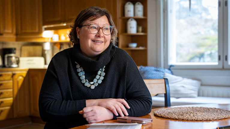 Maria Wasströmn sitter vid ett köksbord, klädd i en svart tröja och ett halsband.