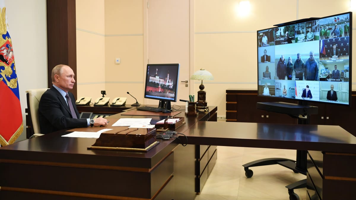 Vladimir Putin istumassa edessään suuri ruutu, jolla näkyy videokokoukseen osallistuvia ihmisiä.
