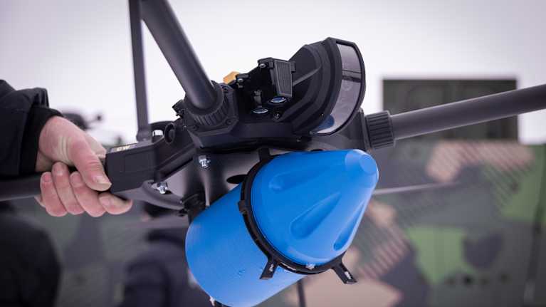 A drone can carry an explosive. The blue object in the picture is not a real explosive but a model. Photo: Juuso Stoor / Yle