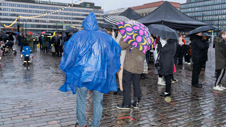 People in raincoats and holding umbrellas in the rain at a market square in Helsinki.