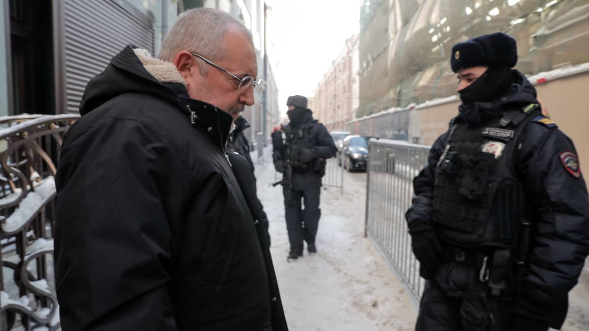 Boris Nadeždin kävelee kapealla kadulla mustassa talvitakissa, jossa on huppu. Kuvan oikeassa laidassa seisoo poliisimies kasvot puoliksi huivin peitossa. Kauempana näkyy toinen poliisi rynnäkkökiväärin kanssa kanssa.