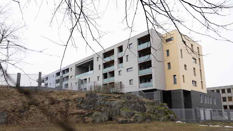 Moderni kerrostalo, jonka edessä on kallioinen rinne ja talvinen maisema.