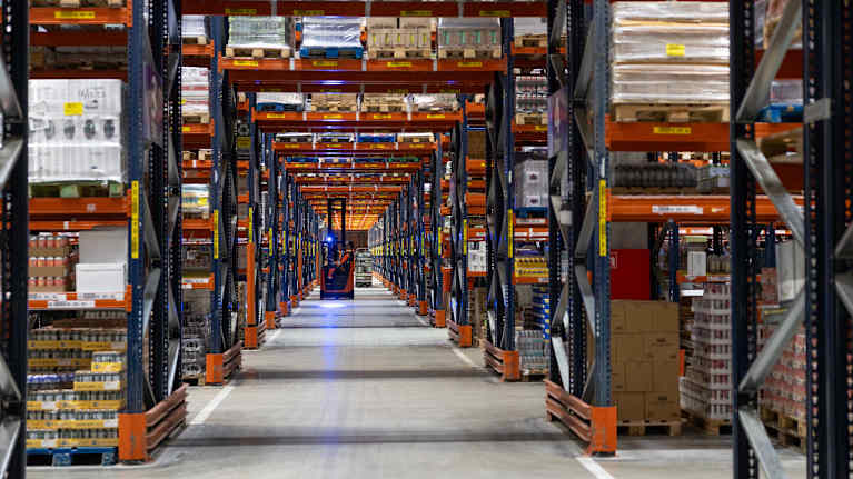 Trukki ajaa sinipunaisten varastohyllyjen keskellä menevällä pitkällä käytävällä. 