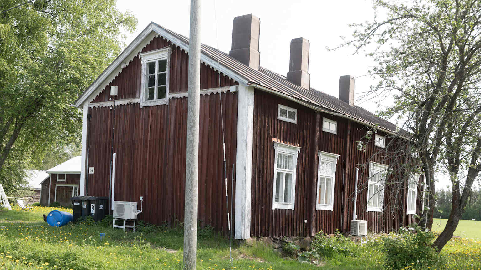 Vanha punaiseksi maalattu, valkoisilla oksilla koristeltu puutalo maaseudulla, vehreyden ja puiden ympäröimänä.