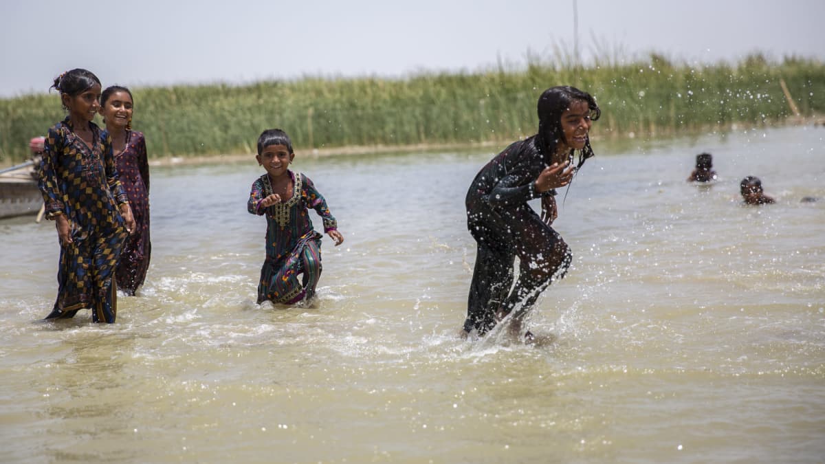 Lapset juoksevat ja ilakoivat vedessä hellekaavut päällään.
