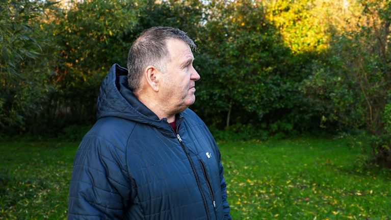 Man tittar åt sidan i trädgård med skog i bakgrunden.