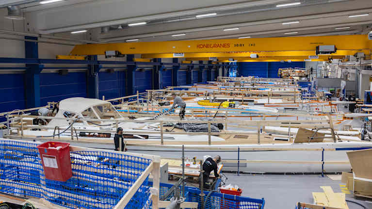 En stor båttillverkningshall med flera personer som arbetar vid långa arbetsstationer och maskiner.
