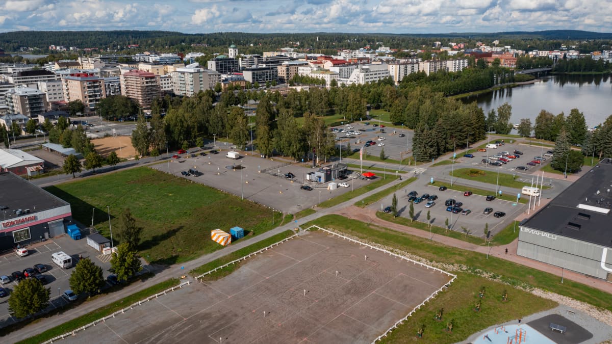 Hämeenlinnan uimahallin parkkipaikalla pysäköityjä autoja. Tyhjä maa-alue odottamassa rakentamista. 