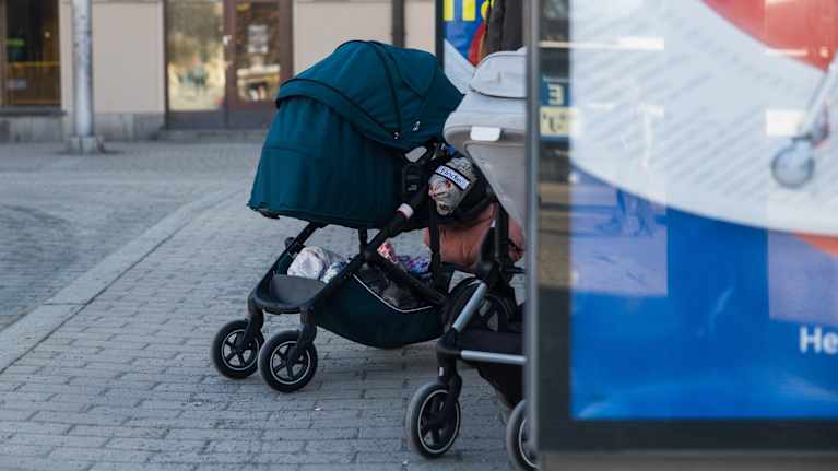 Two baby buggies on a city sidewalk.