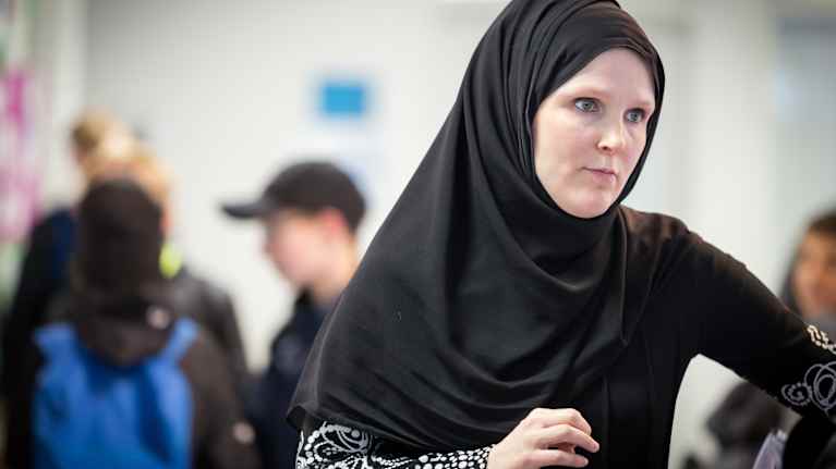 Woman wearing a black headscarf, with young people seen in the background.