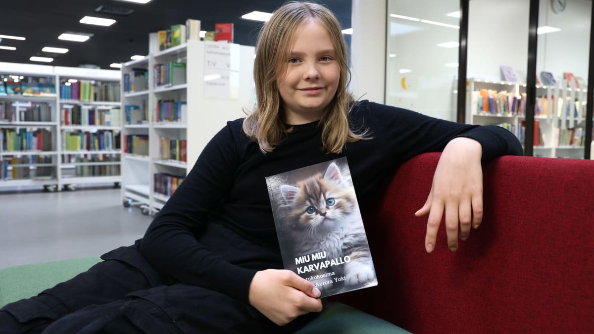 10-vuotias Armi Yoki istuu kirjaston sohvalla pitäen kädessä kirjoittamansa Miu Miu Karvapallo -kirjaa, jonka kannessa on pörröinen kissanpentu.