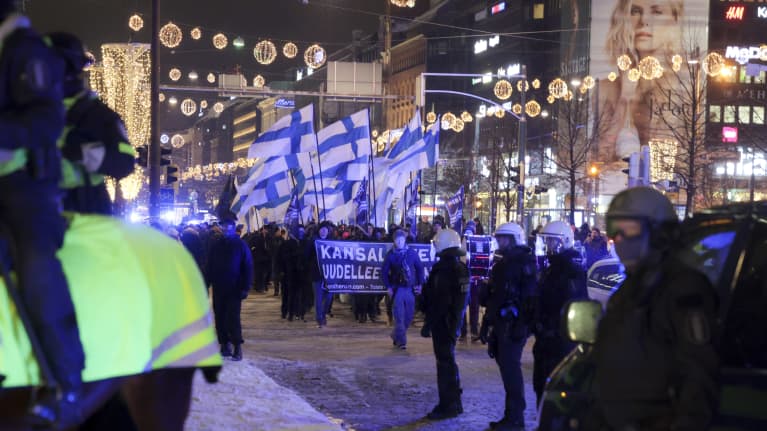 Suomi Herää -kulkue kulkee lumisessa maassa Suomenliput pystyssä. Poliisit valvovat.
