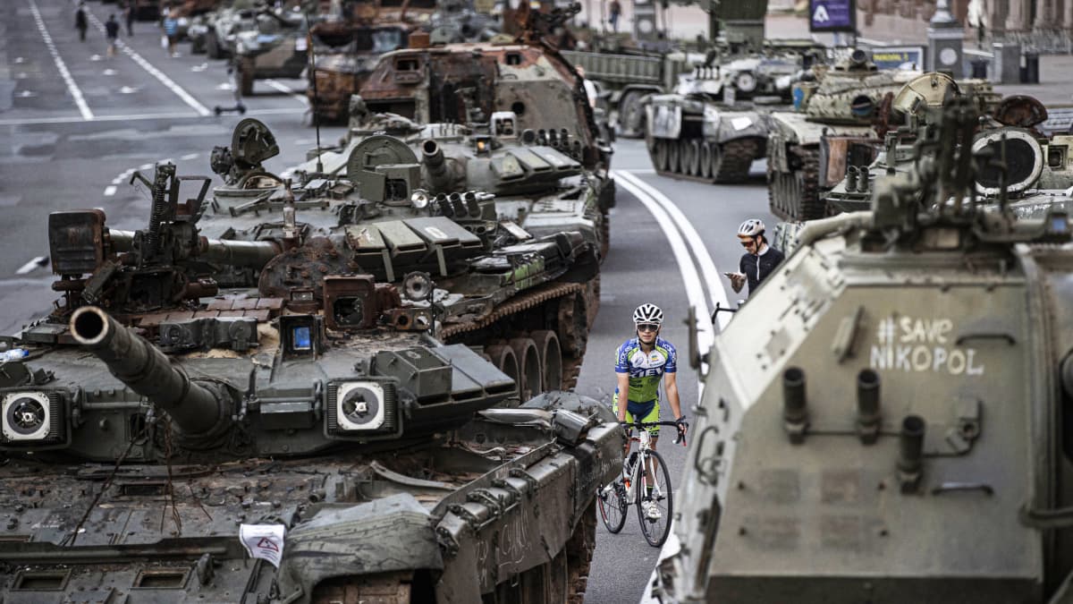 Pyöräilijä venäläisten takavarikoitujen tankkien välissä.