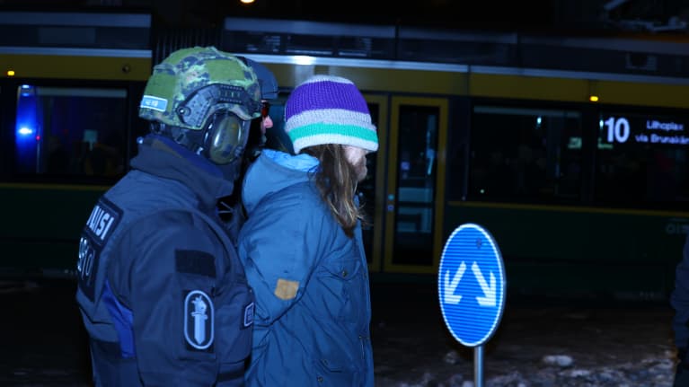 Poliisi taluttaa mielenosoittajaa jolla on pipo silmillä.