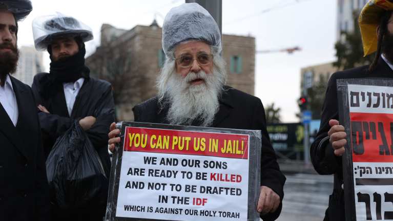 Haredijuutalainen mies pitää kädessään kylttiä: "You can put us in jail! We and our sons are ready to be killed and not to be drafted in the IDF which is against our holy Torah"