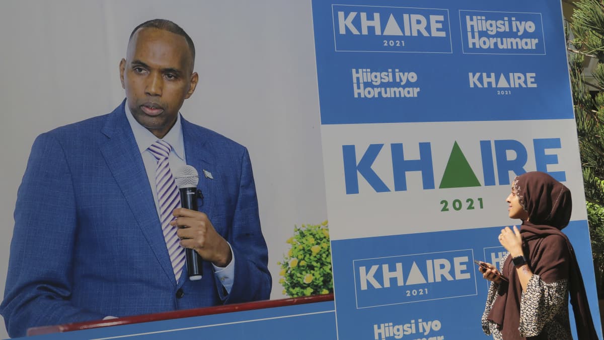 Somalialainen hunnutettu nainen katsoo läheltä suurta sinisävyistä vaalimainosta, jossa suurena siniseen pukuun ja siniraidalliseen kravattiin pukeutunut presidenttiehdokas Ali Khaire. 