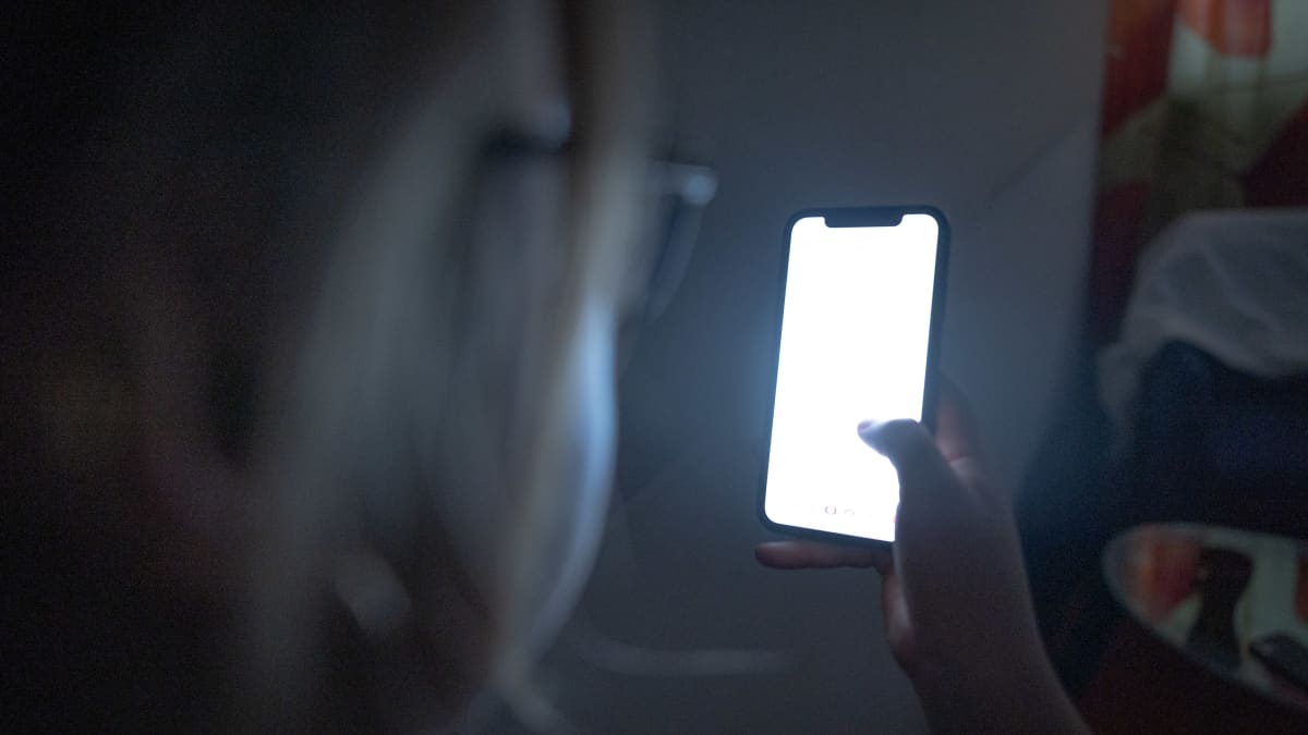 An anonymous youth looks at their phone in the dark