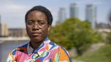 Jenny Kasongo katsoo kameran ohi, taustalla vihreä puu ja Kalasataman tornitalot.