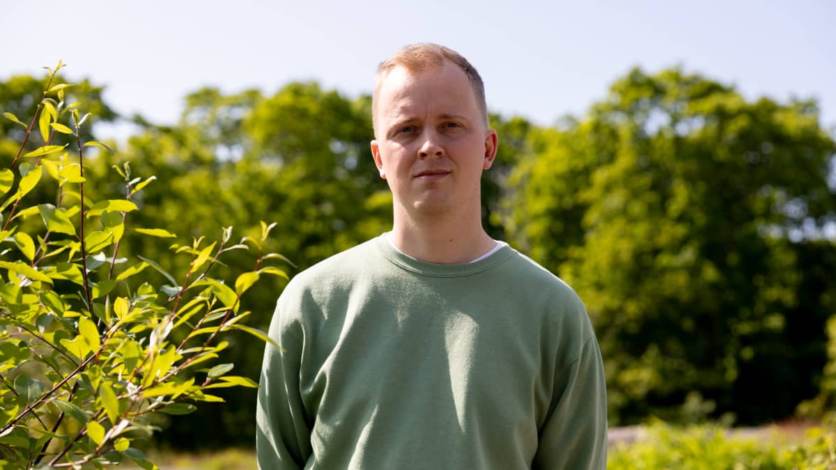 Ilmatieteenlaitoksen tutkija Mika Rantanen katsoo kameraan. Vieressä vehreä pensas ja takana kauempana puita.