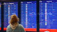 Blurred rear view of a woman looking at a large electronic departures board at an airport. 