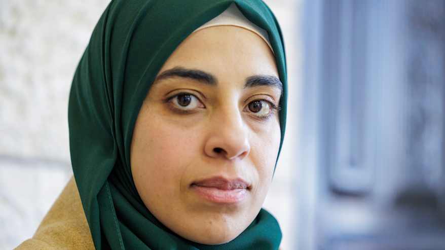 Musliminainen vihreä huivi päässään katsoo totisena kameraan.