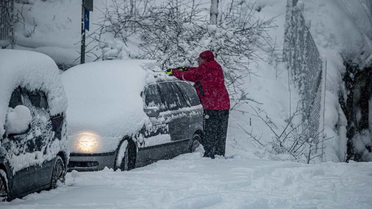 Henkilö putsaa autoa lumesta.