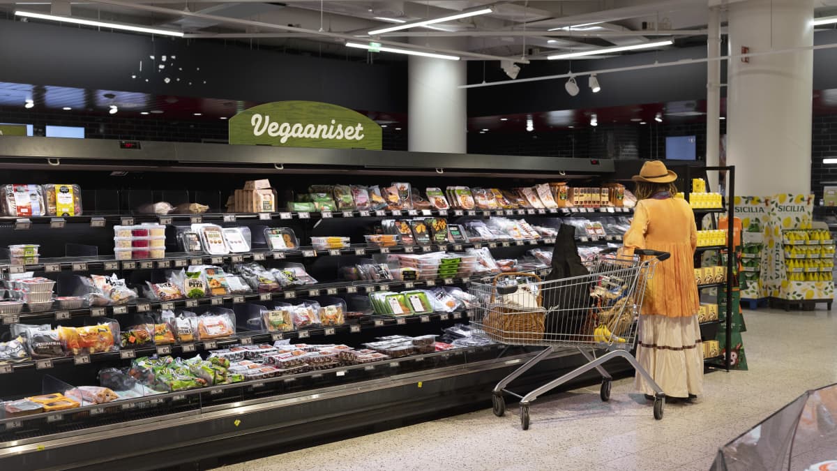 Woman looking at a supermarket's refrigerated section containing vegan products.