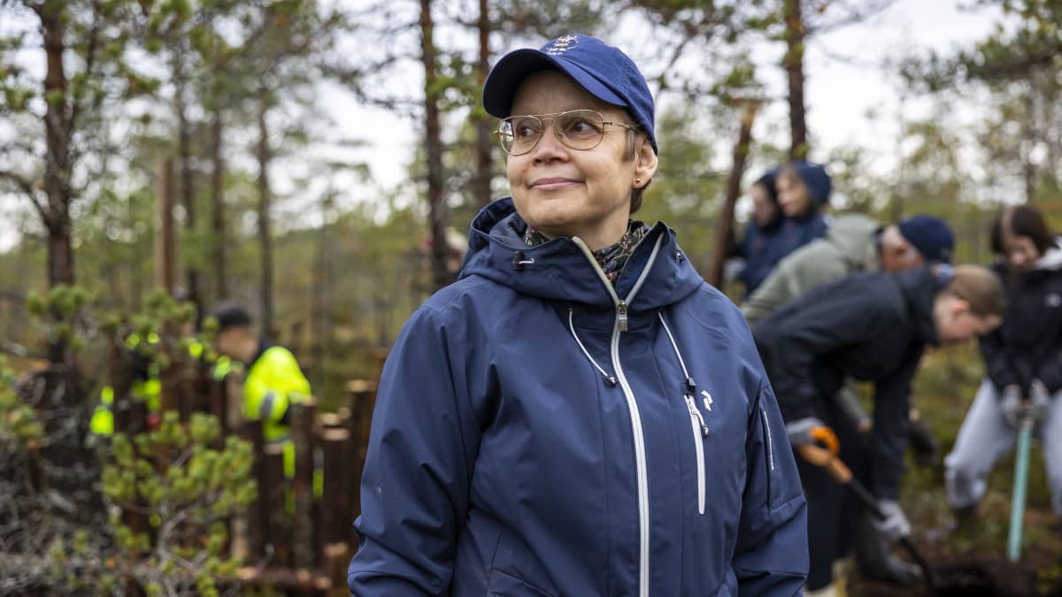 Opettaja Anna-Liisa Peltonen seisoo suolla. Takana oppilaita lapioimassa suota.