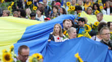 Joukko ihmisiä kantaa suurta Ukrainan lippua ja auringonkukkia.