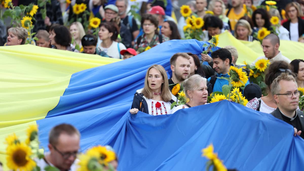 Joukko ihmisiä kantaa suurta Ukrainan lippua ja auringonkukkia.