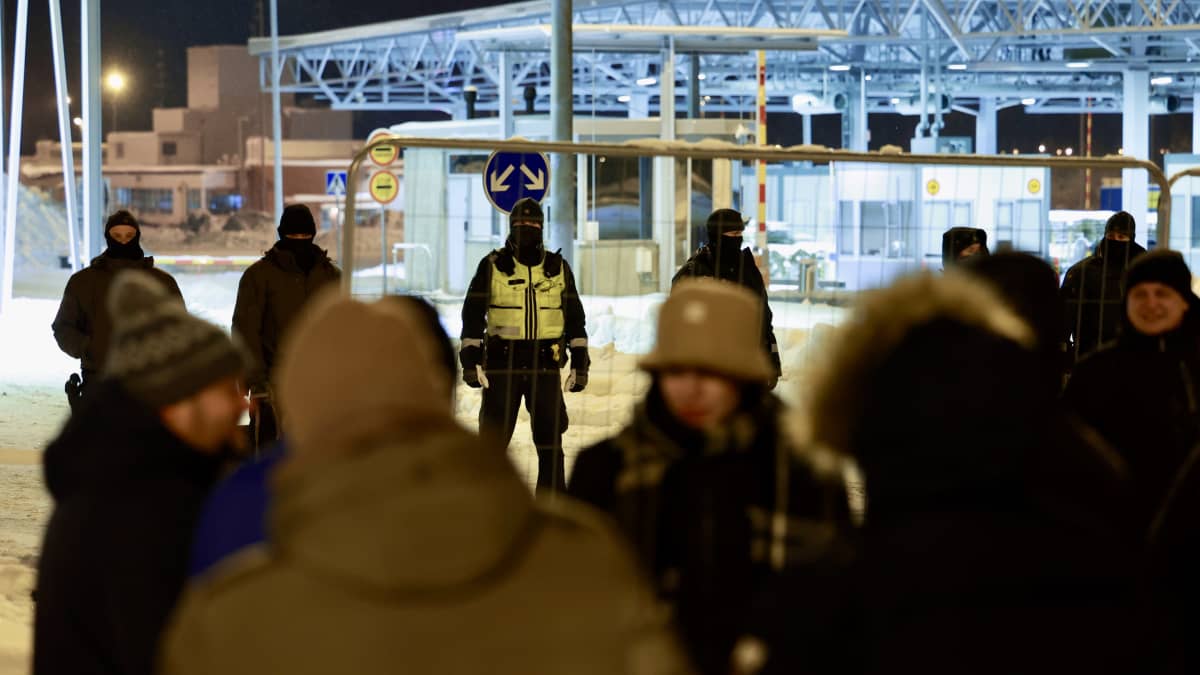 Joukko poliiseja ja viranomaisia seisoo nk. festariaidan takana lumimaisemassa. Toisella puolella seisoo ihmisiä talvivaatteissa.