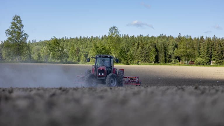 Traktori ajaa pellolla. Pölyä nousee ilmaan.