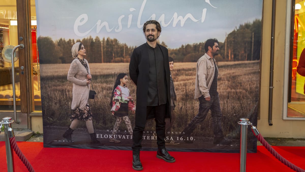 Elokuvaohjaaja Hamy Ramezan poseeraa punaisella matolla Ensilumi-elokuvansa julisteen edessä (kokokuva).