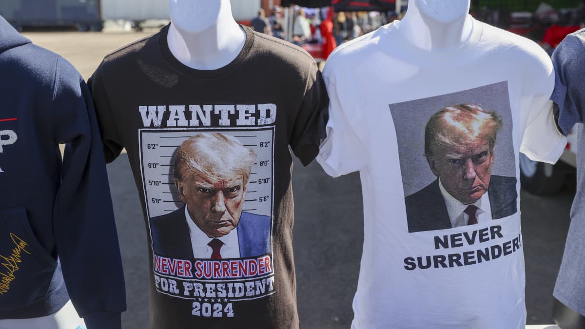Trumpin pidätyskuva kahdessa erilaisessa t-paidassa. Teksti Never surrender. 