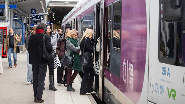 People on a train platform, seen from the side, boarding a purple and white local train.