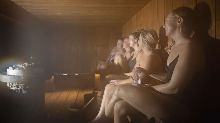 Viisi naista istuu vierekkäin höyryn keskellä Matinkylän konttisaunassa.