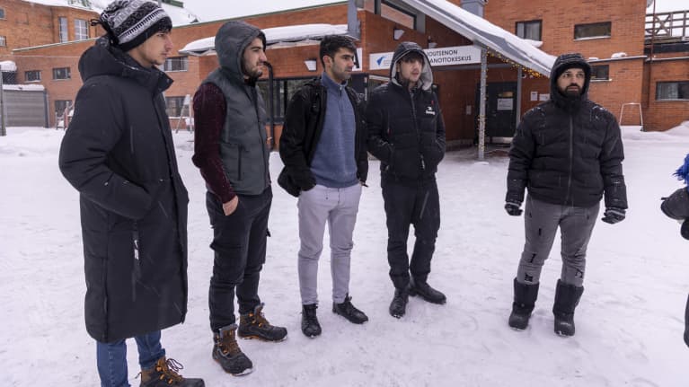 A group of men stand in front of a reception centre in a wintry landscape.