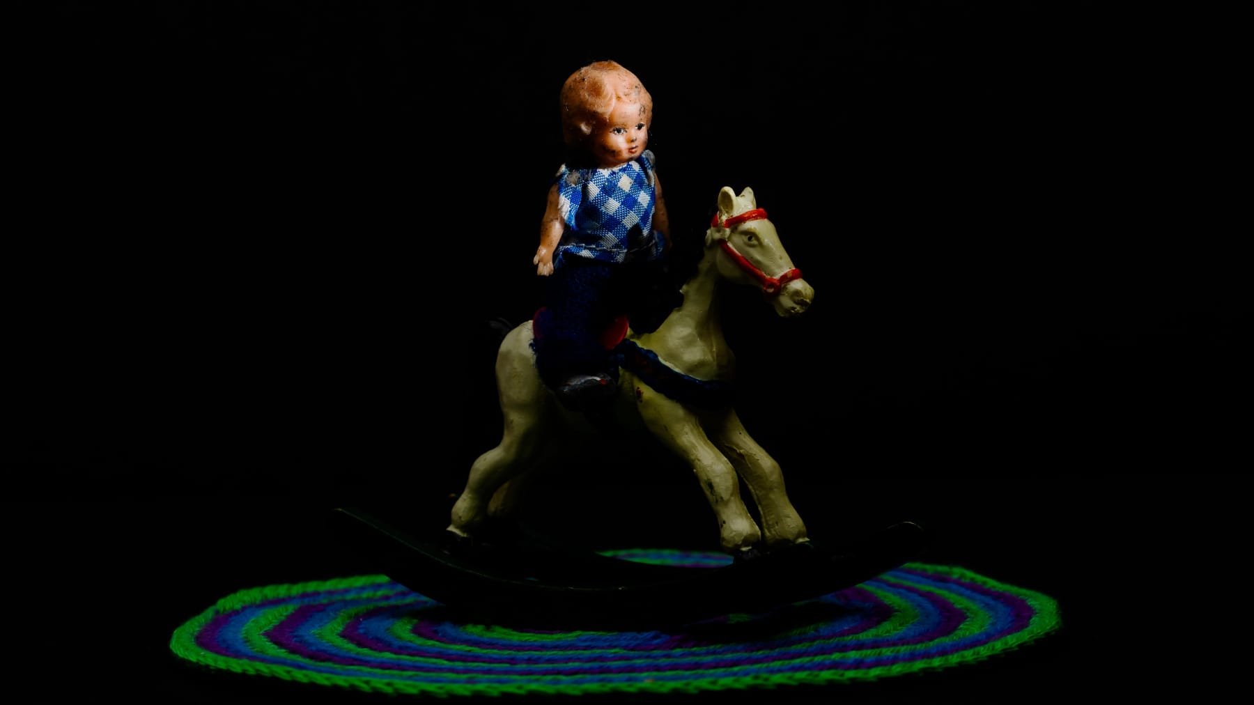 Miniatyyrinukke ratsastaa keinuhevosella.