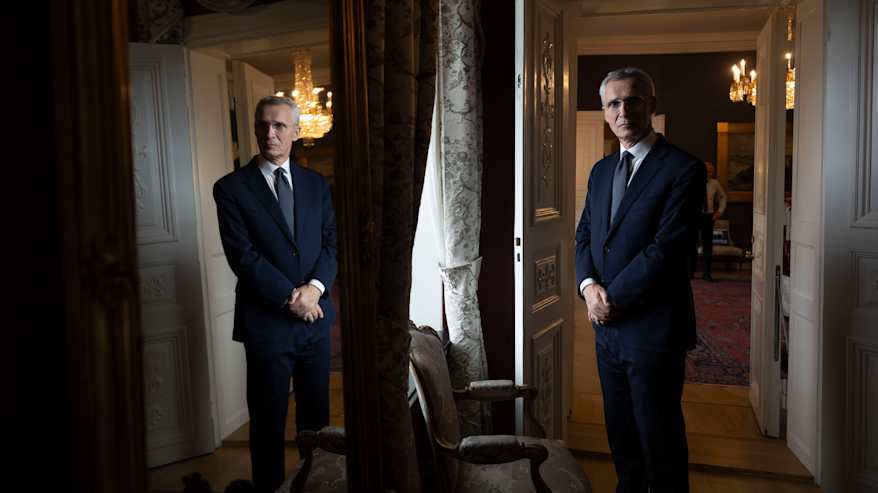  Jens Stoltenberg seisoo ikkunan edessä puku päällä. Viereisestä peilistä heijastuu Stoltenbering kuvajainen.