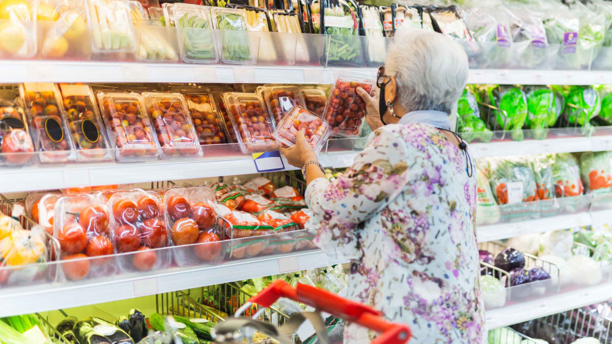 En gammal kvinna fotograferad bakifrån medan hon handlar mat i mataffär.