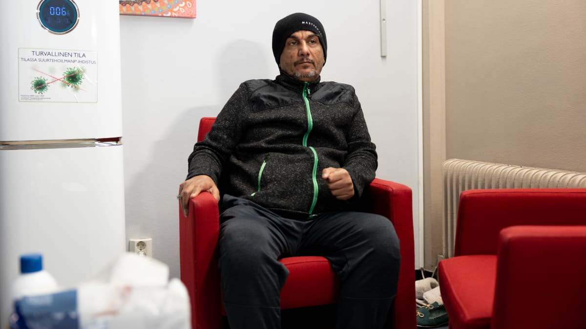Adnan Houssain istuu punaisessa tuolissa ja  katsoo kameran ohi. Päässä on musta pipo.