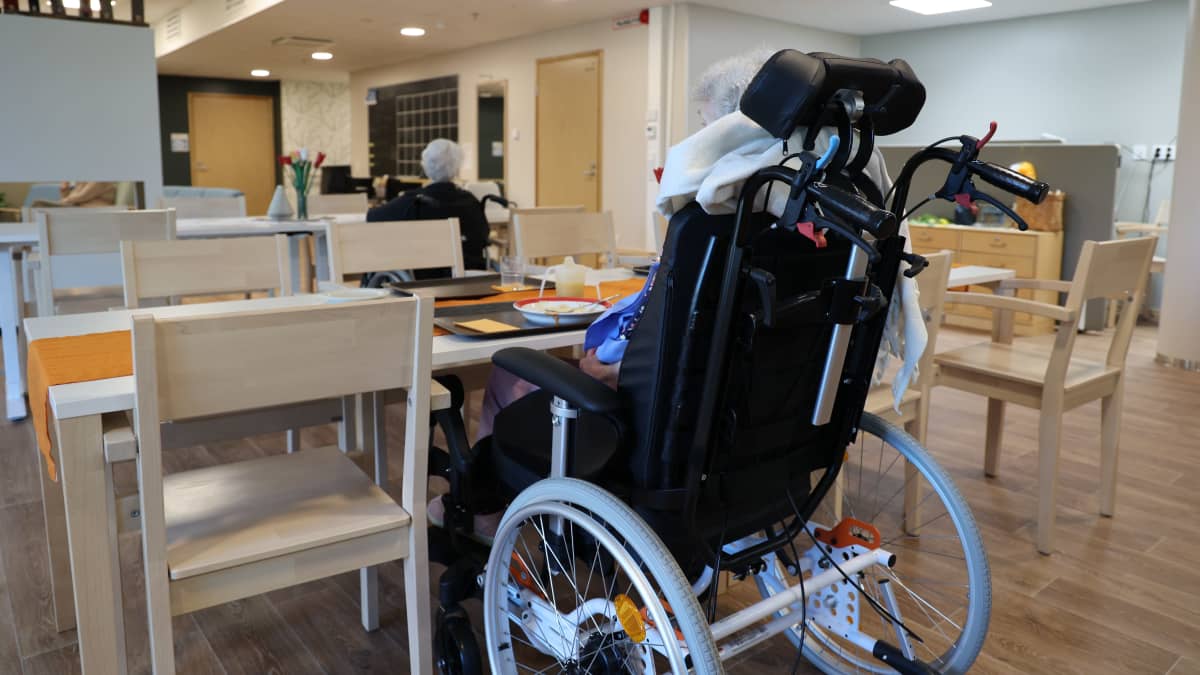 Kaksi vanhusta istuu ruokapöydän ääressä takaapäin kuvattuna palvelutalossa.