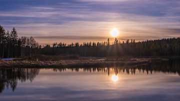Ilta-aurinko paistaa Taivalkoskella upeasti tyynen järven pintaan.