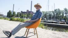 Ydinvoiman mallinnuksen professori Juhani Hyvärinen istuu oranssilla tuolilla Hanasaaren voimalan edustalla.