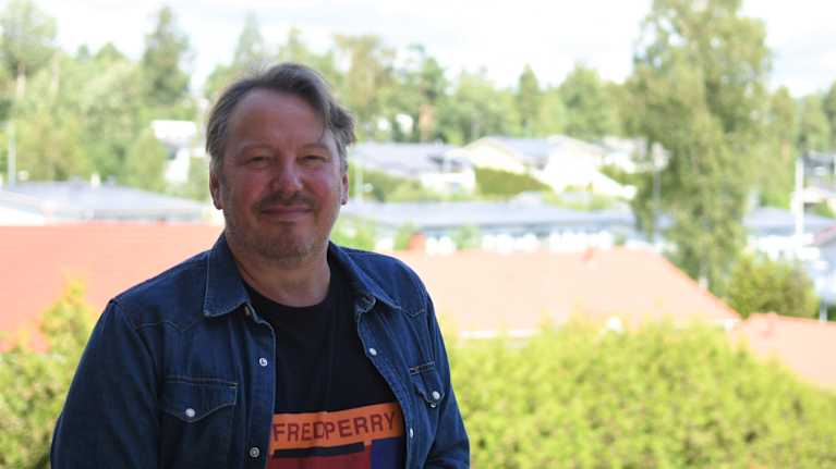 Man som står ute i solskenet och ler.