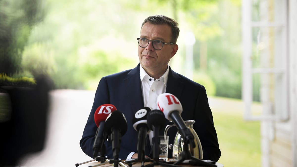 Petteri Orpo tiedotustilaisuudessa seisoo median mikrofonit edessään korkean pöydän edessä.